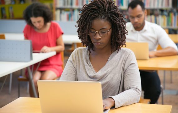 Front view of concentrated woman working with laptop at library. Focused African American woman typing on laptop. Technology concept